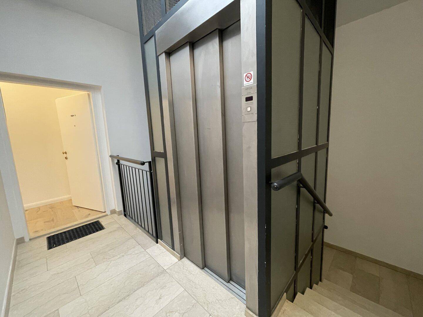 Eingangsbereich mit modernem Aufzug und Treppenhaus, ausgestattet mit Fliesenboden.