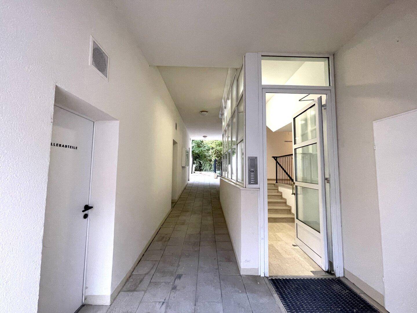 Überdachter Außenflur mit Fliesenboden und Zugangsbereich mit Rampe und Treppe.