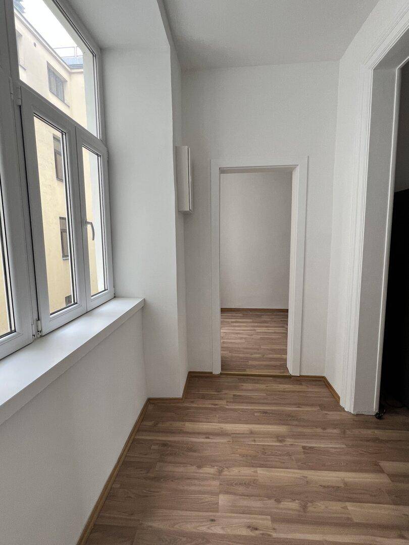 Heller Flur mit Laminatboden und großem Fenster, das den Blick auf einen Innenhof freigibt.