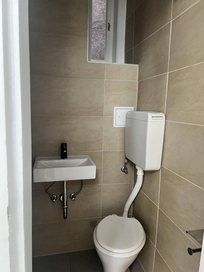 Kleines Gäste-WC mit beigefarbenen Fliesen, Toilette, Waschbecken und einem kleinen Fenster.