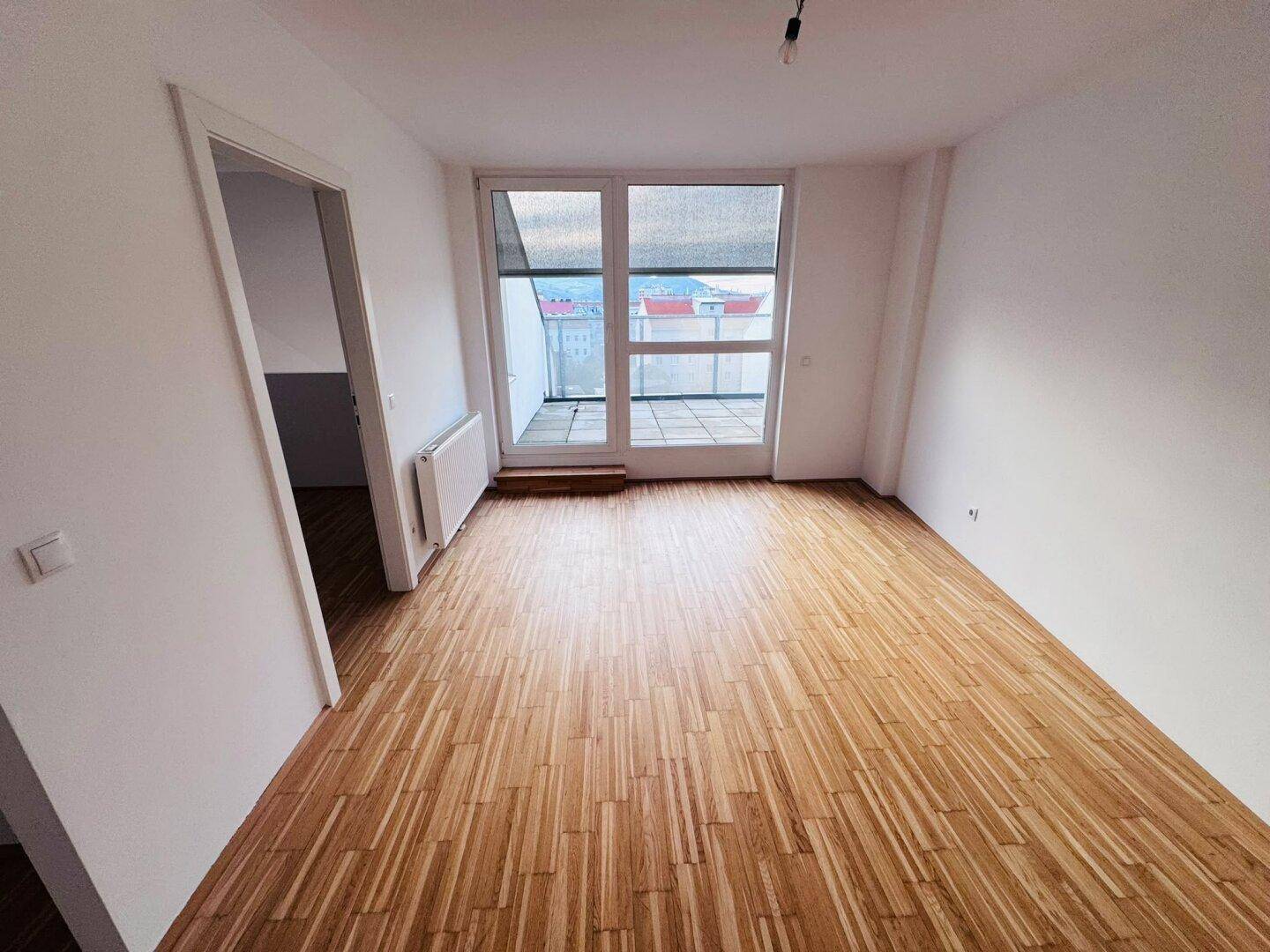 Geräumiges Wohnzimmer mit Parkettboden und großen Fenstern, die viel Licht hereinlassen.