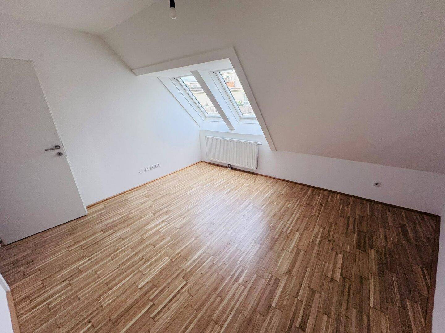 Schlafzimmer im Dachgeschoss mit Parkettboden, Dachschrägen und einem Dachfenster für Tageslicht.