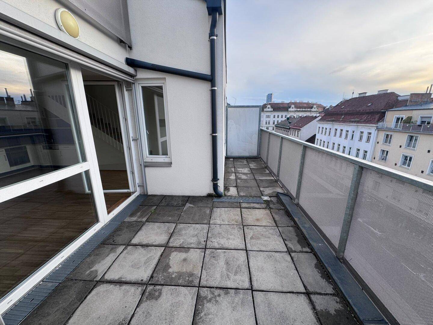 Geräumige Dachterrasse mit Fliesenboden und Metallgeländer, bietet einen Blick über die Stadt.