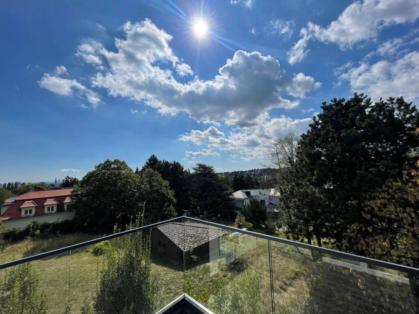 Weitläufiger Ausblick von der Terrasse mit viel Grün und strahlendem Sonnenschein am blauen Himmel.
