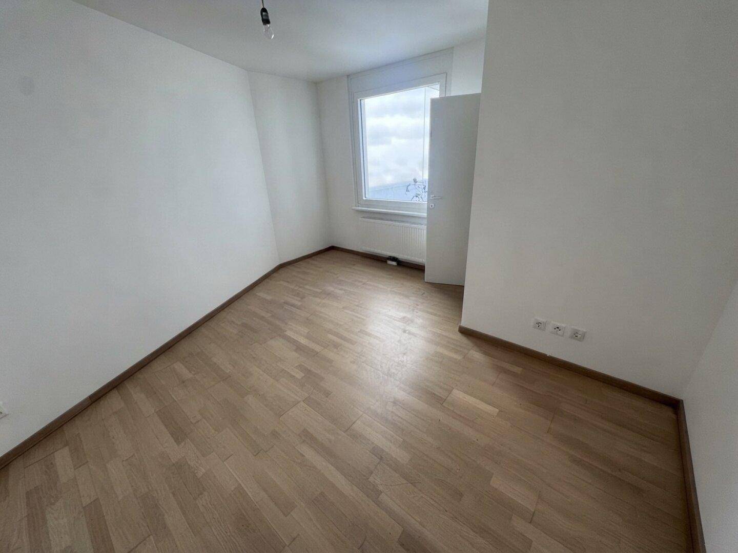Helles Schlafzimmer mit Parkettboden und einem Fenster, das einen Blick ins Grüne bietet.