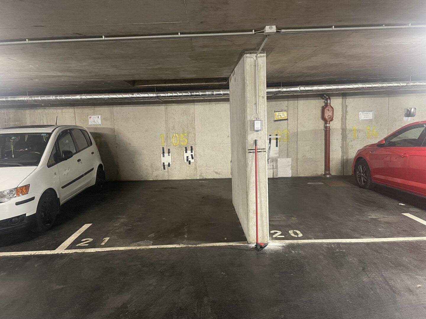Tiefgarage mit markierten Parkplätzen und rotem Feuerlöscher an der Betonwand.