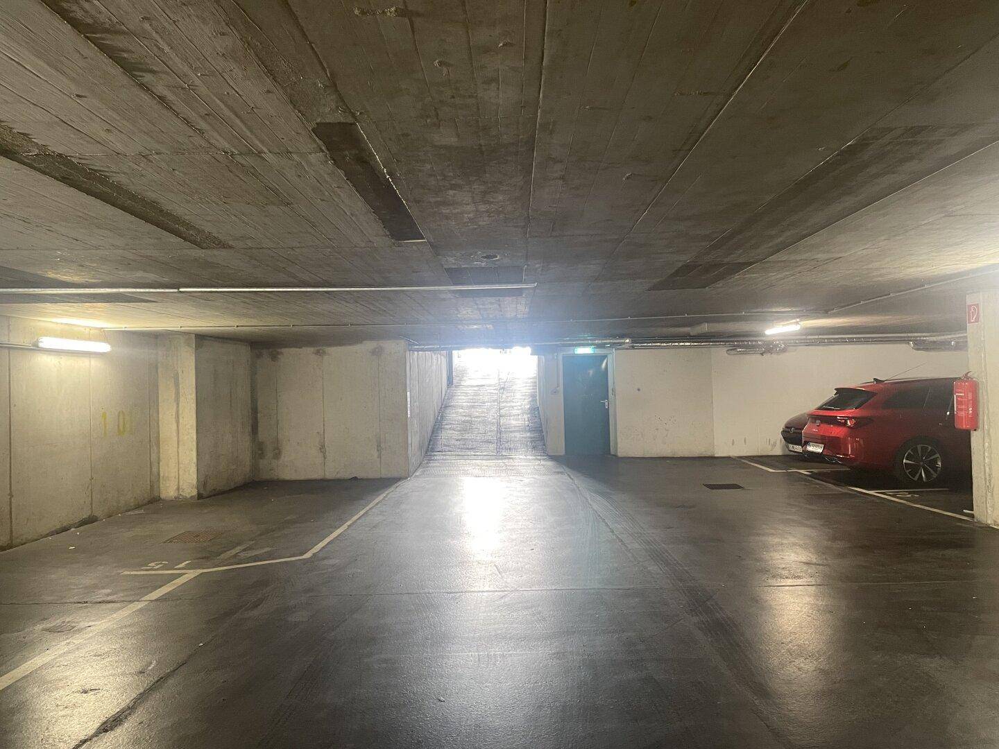 Geräumige Tiefgarage mit Betonwänden und -decke, die zu einer hellen Ausfahrt führt.