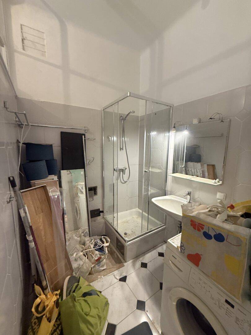 Kleines Badezimmer mit Duschkabine, Waschbecken und Waschmaschine, renovierungsbedürftig.