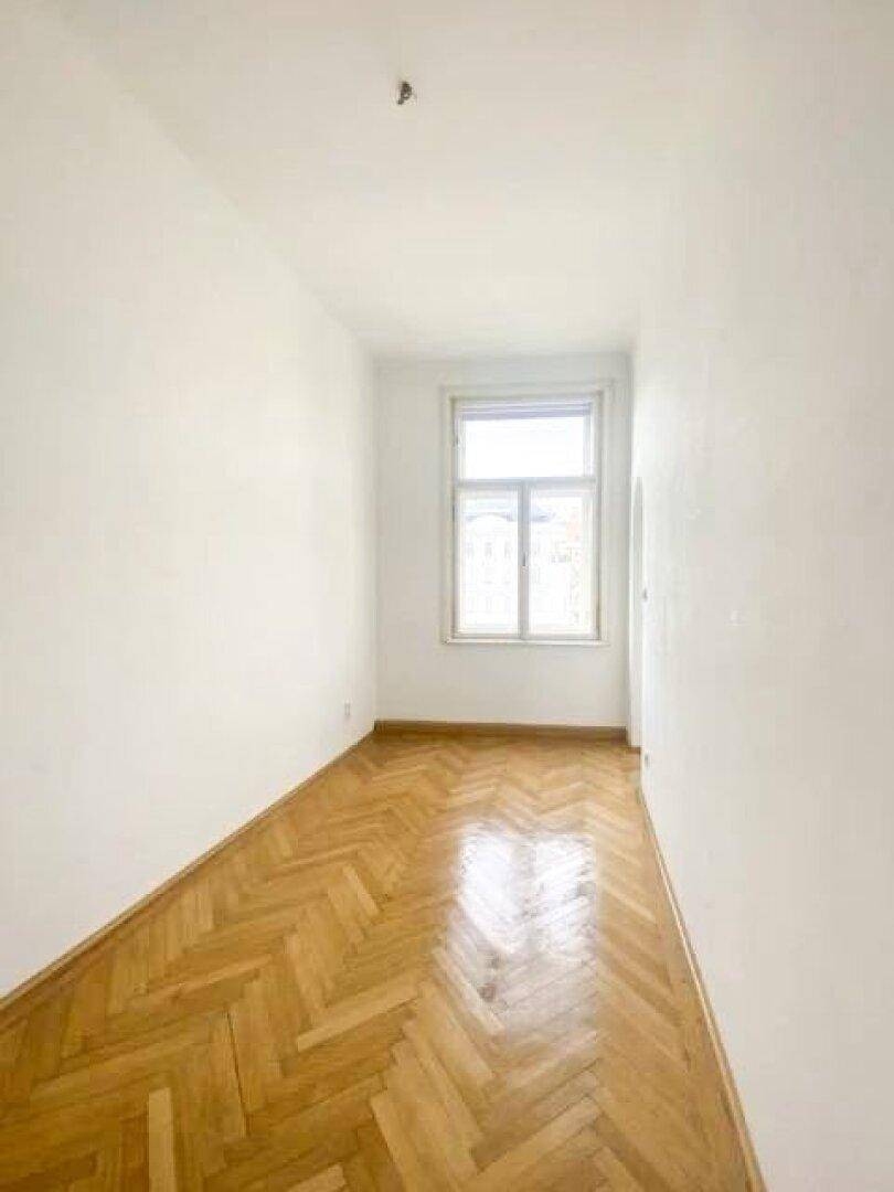 Schmales, helles Zimmer mit Fischgrätparkett und einem Fenster.