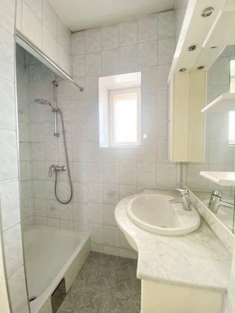 Badezimmer mit Duschwanne, Waschbecken, Spiegelschrank und hellen Fliesen.