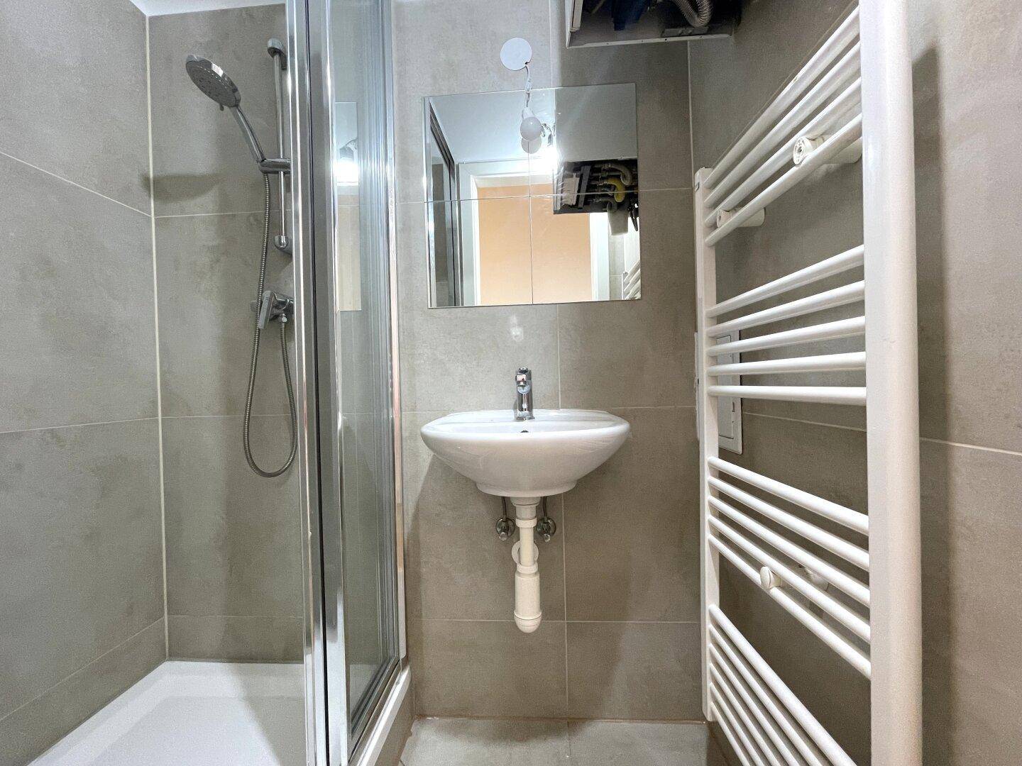 Modernes Badezimmer mit Duschkabine, Waschbecken und beheiztem Handtuchhalter.