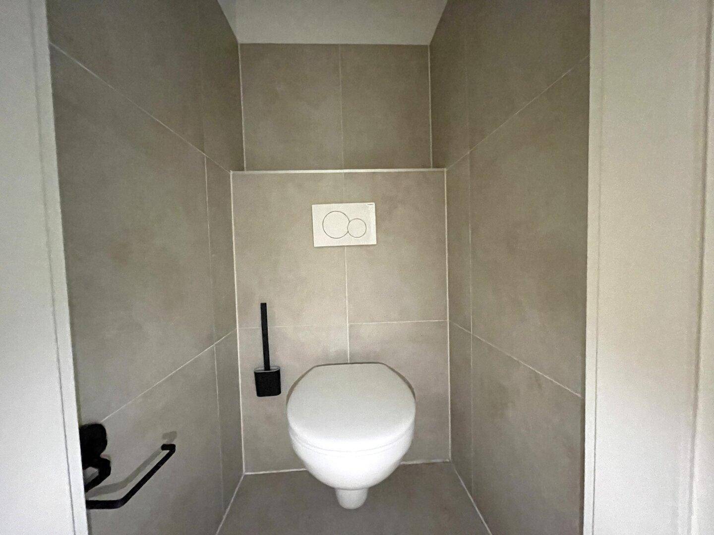 Separates WC mit wandhängender Toilette und modernen grauen Fliesen.