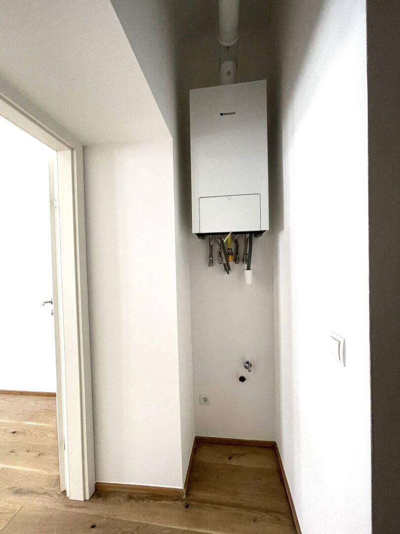 Kleiner Bereich mit Warmwasserbereiter an der Wand und Holzboden.