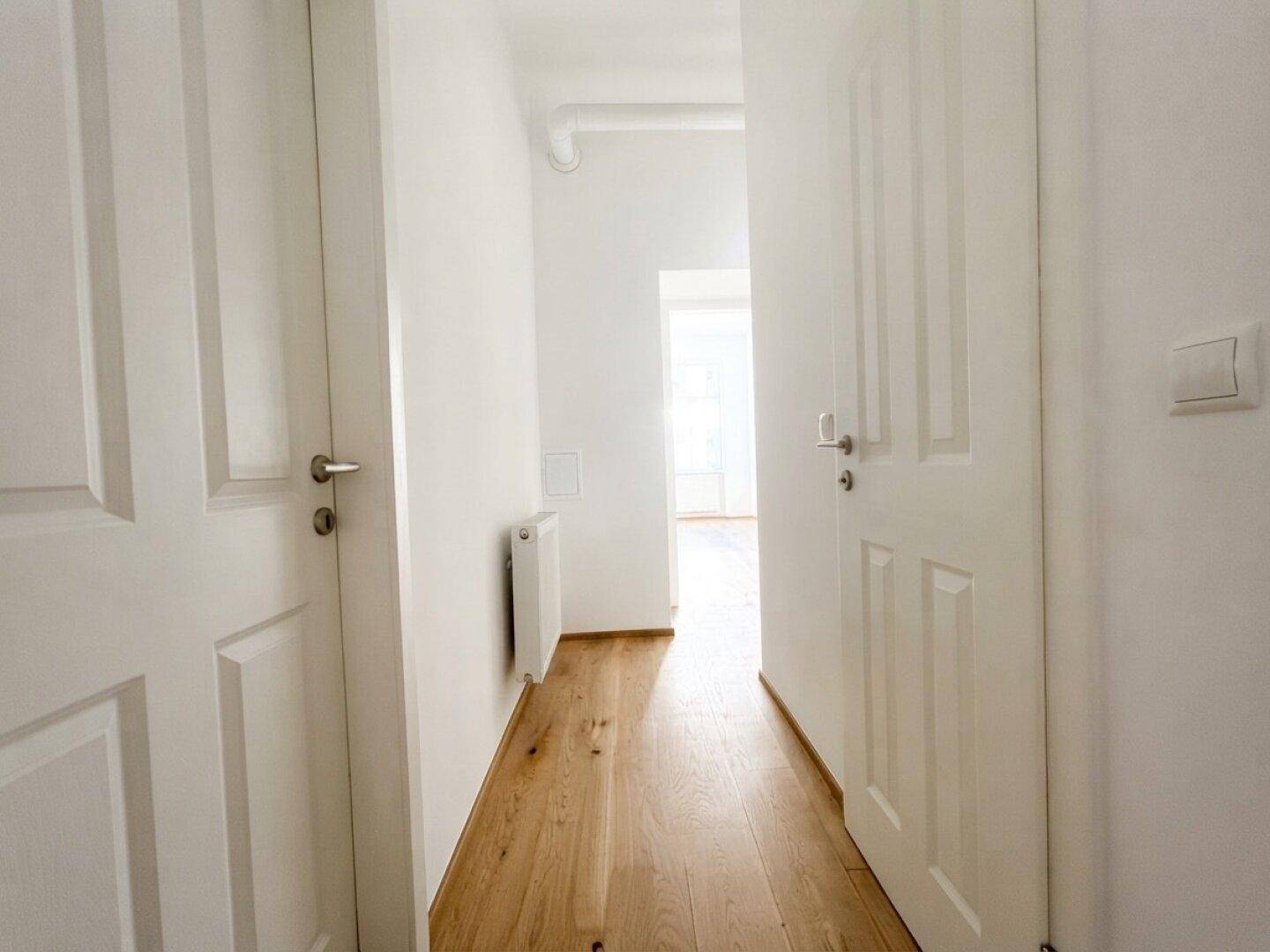 Heller Flur mit Holzboden und weißen Türen, der zu weiteren Räumen führt.