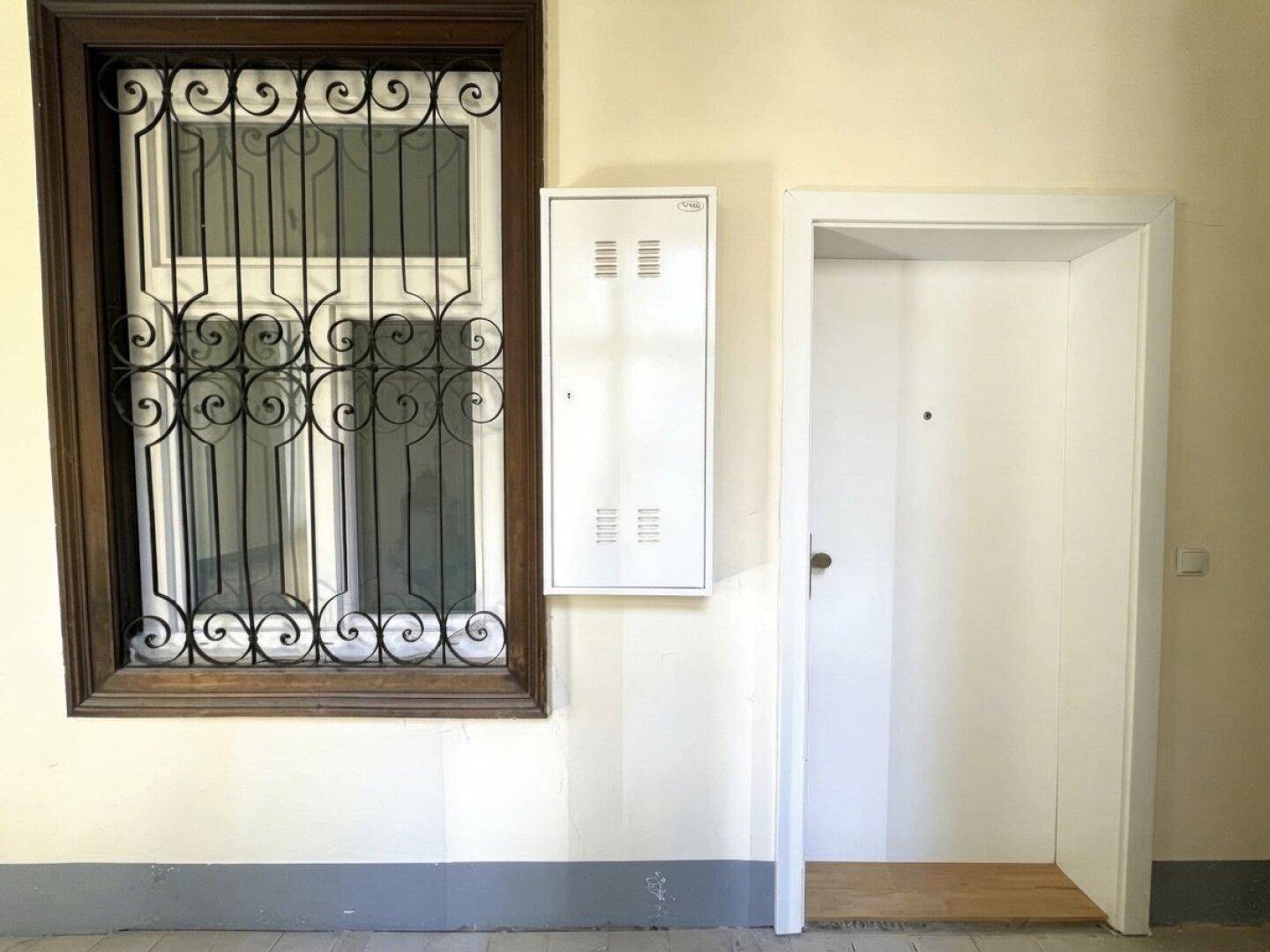 Eingangsbereich des Gebäudes mit weißer Tür und Fenster mit schmiedeeisernem Gitter.
