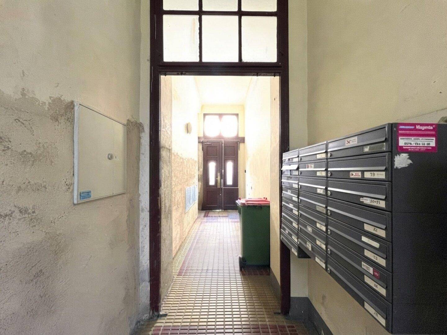 Eingangsbereich eines Altbaus mit Briefkästen, originalem Fliesenboden und Blick zum Haupteingang.