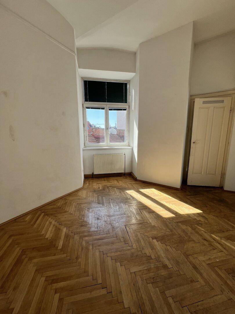 Heller Raum mit Fischgrätparkettboden, weiß gestrichenen Wänden und natürlichem Lichteinfall durch das Fenster.