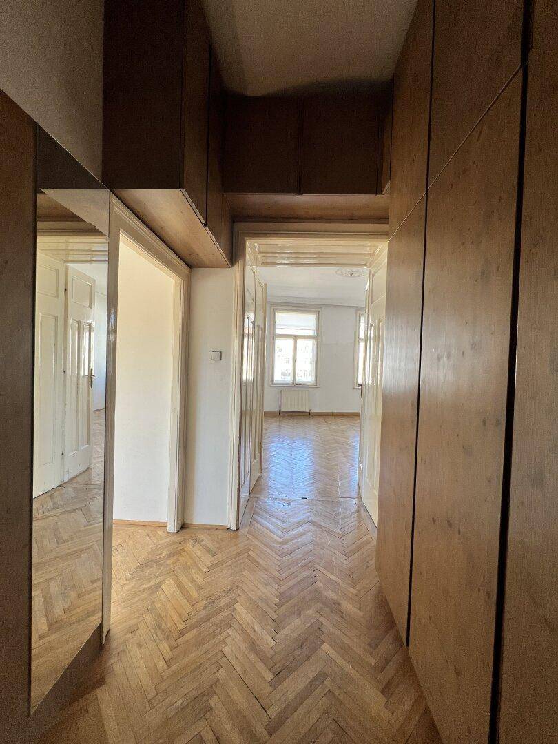 Langer Flur mit integrierten Holzschränken, Spiegeln und durchgehendem Fischgrätparkettboden.