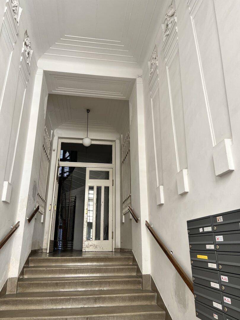 Eingangsbereich eines Mehrfamilienhauses mit Treppe, Briefkästen und dekorativen Wandelementen.