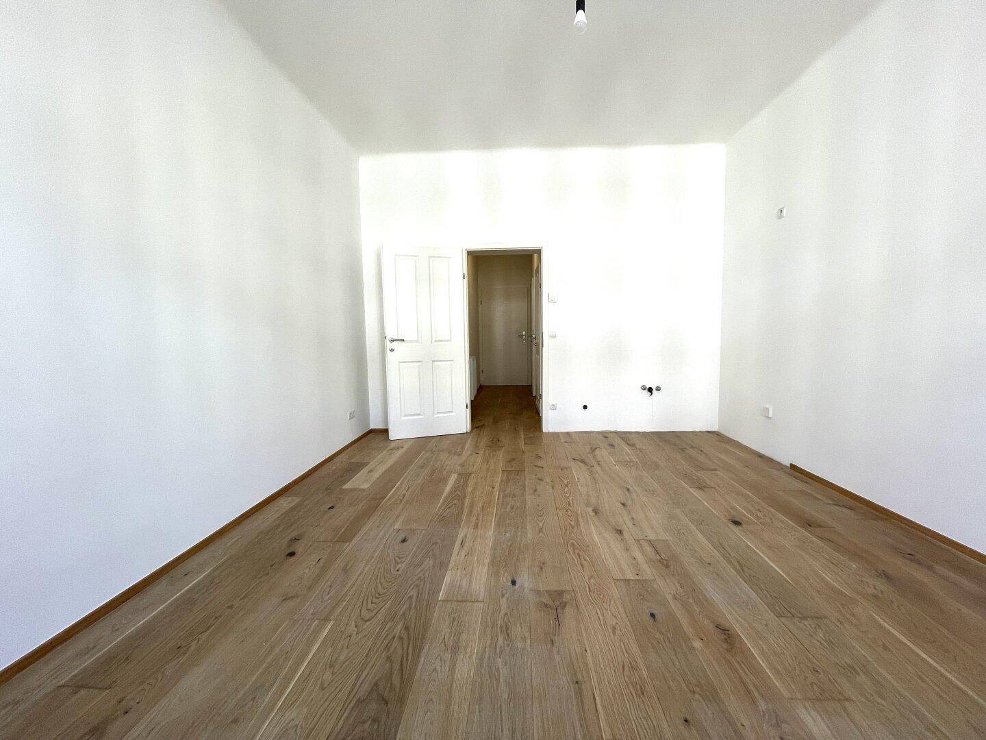 Geräumiges Zimmer mit hellem Holzplankenboden und weiß gestrichenen Wänden, ideal für Wohnzwecke.