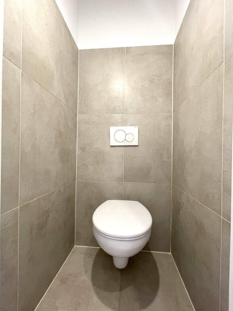 Modernes separates WC mit wandhängender Toilette und großformatigen grauen Fliesen.