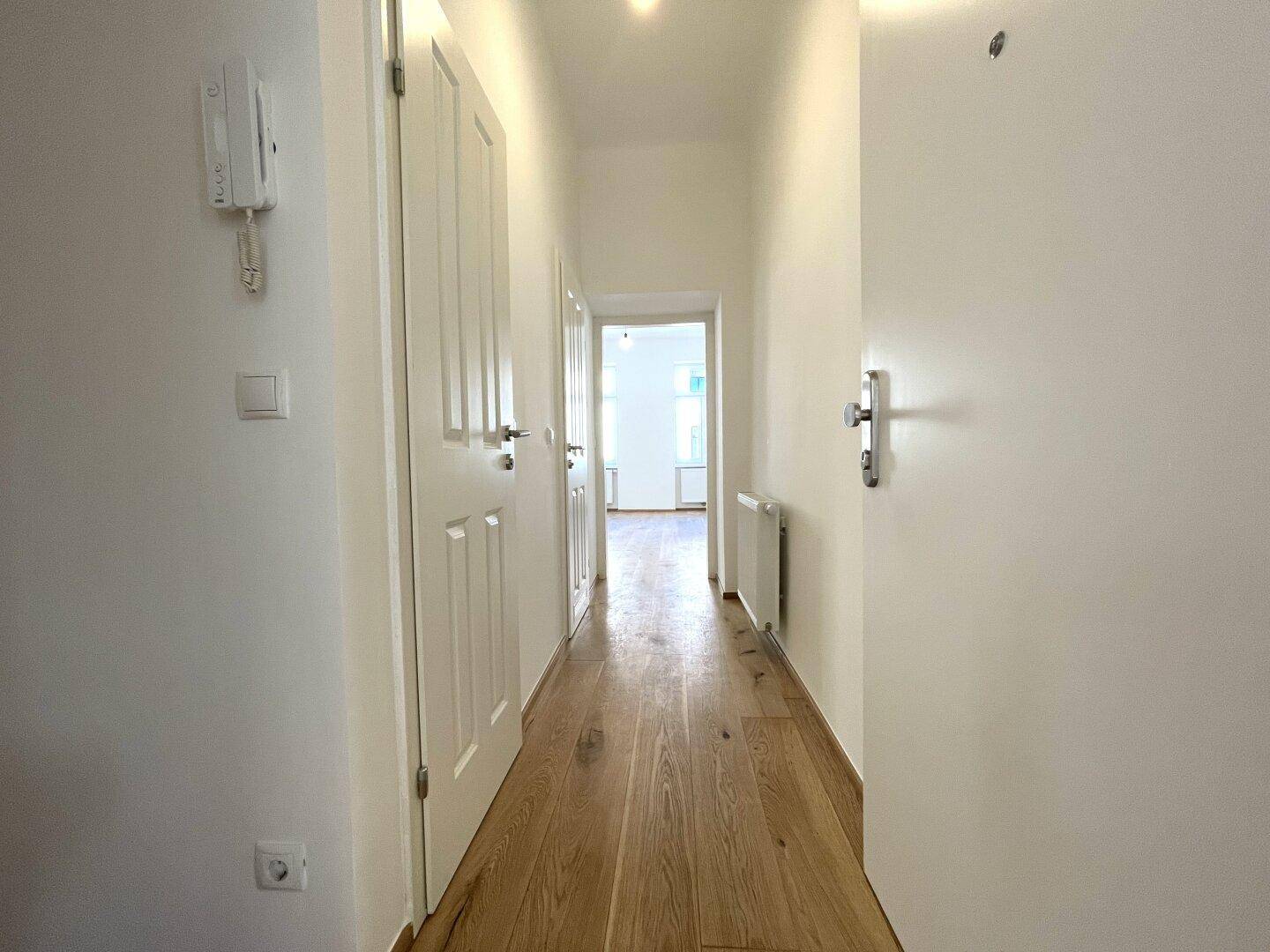 Heller Flur mit Holzplankenboden und mehreren Türen, ausgestattet mit einer Gegensprechanlage.