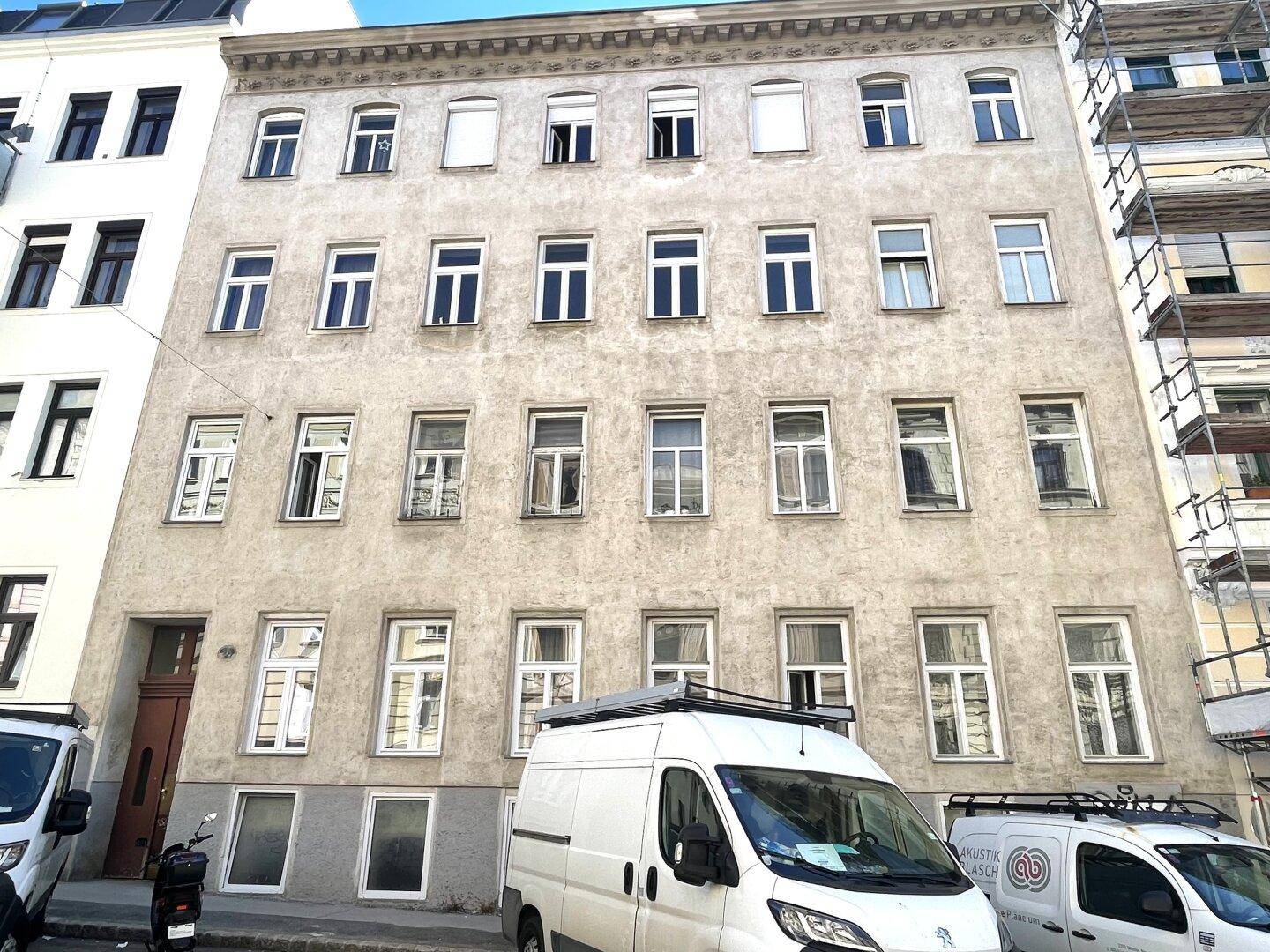 Fassade eines Mehrfamilienhauses mit zahlreichen Fenstern und Anzeichen von Renovierungsarbeiten.