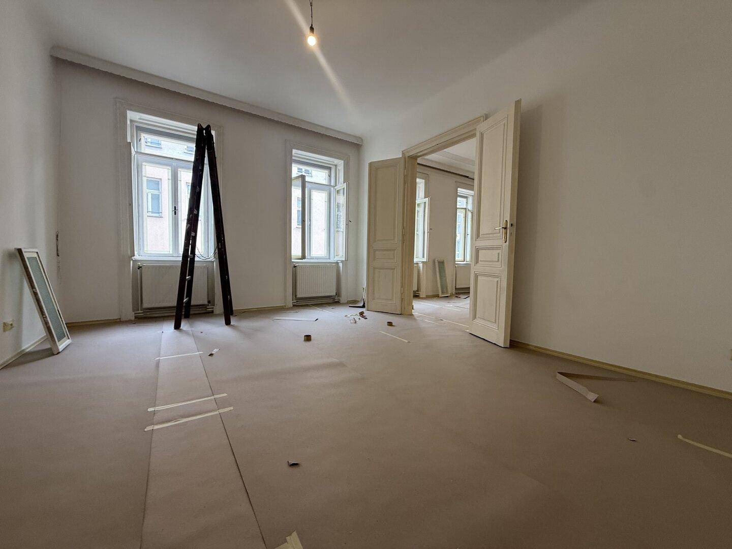 Großer Raum in Renovierung mit hohen Decken und geöffneten Doppeltüren.