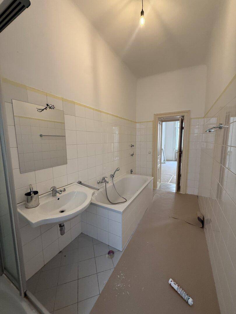 Helles Badezimmer mit weißen Fliesen, Badewanne, Waschbecken und Duschbereich.