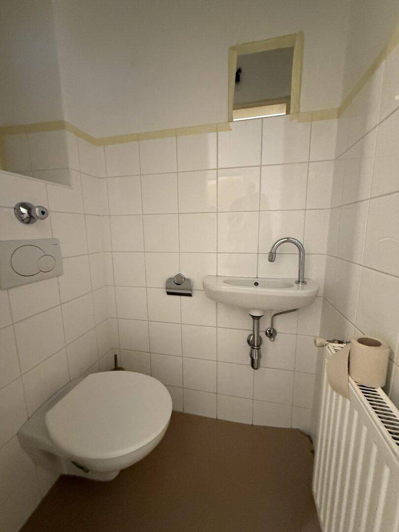 Kleines Gäste-WC mit Wand-WC, kleinem Waschbecken und Heizkörper.