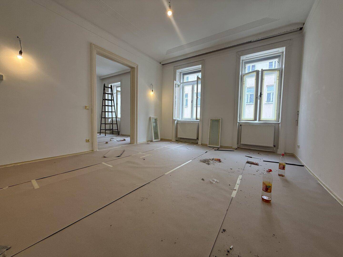 Geräumiger Raum in Renovierung mit hohen Decken und zwei großen Fenstern, bereit für die Gestaltung.