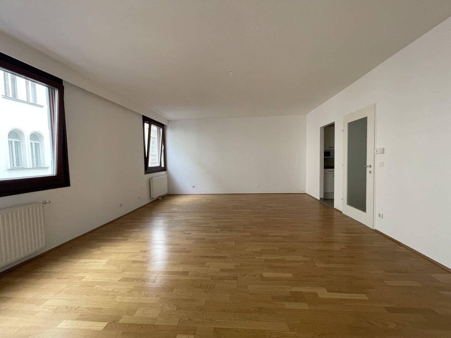 Helles und geräumiges Wohnzimmer mit Parkettboden und zwei großen Fenstern.