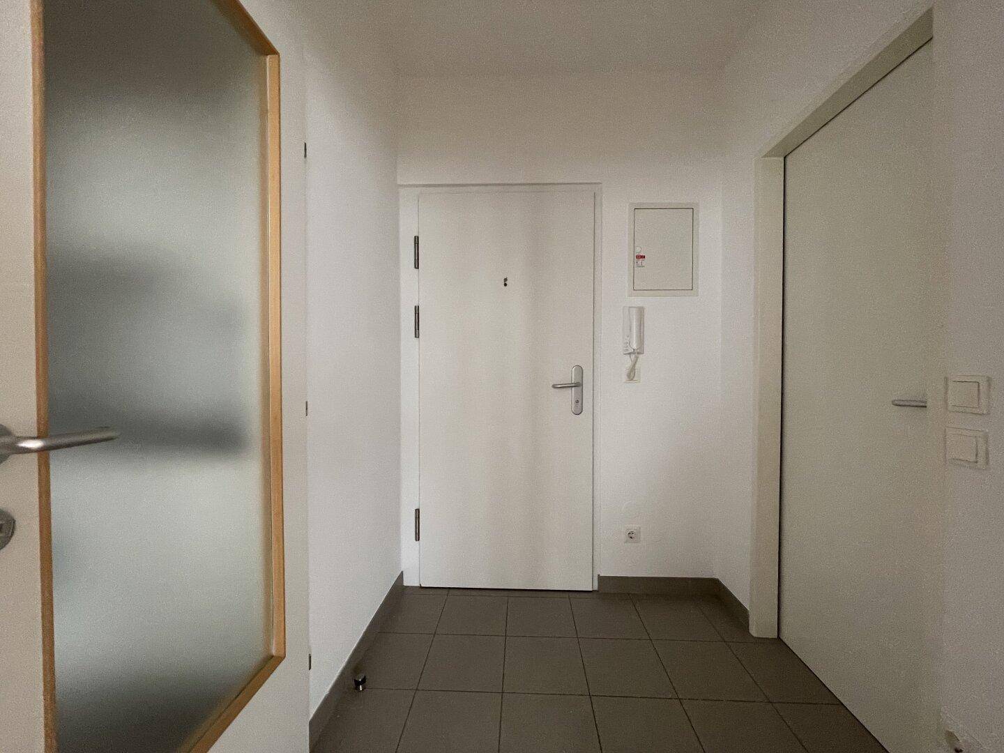 Heller Eingangsbereich einer Wohnung mit Fliesenboden und weißen Türen.