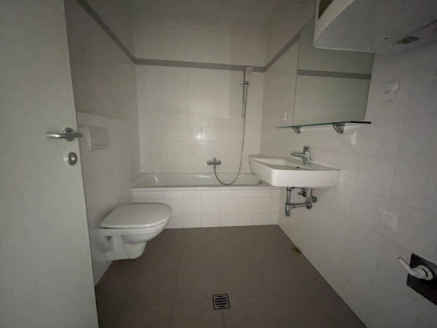 Badezimmer mit weißen Fliesen, Badewanne mit Duschfunktion, Toilette und Waschbecken.