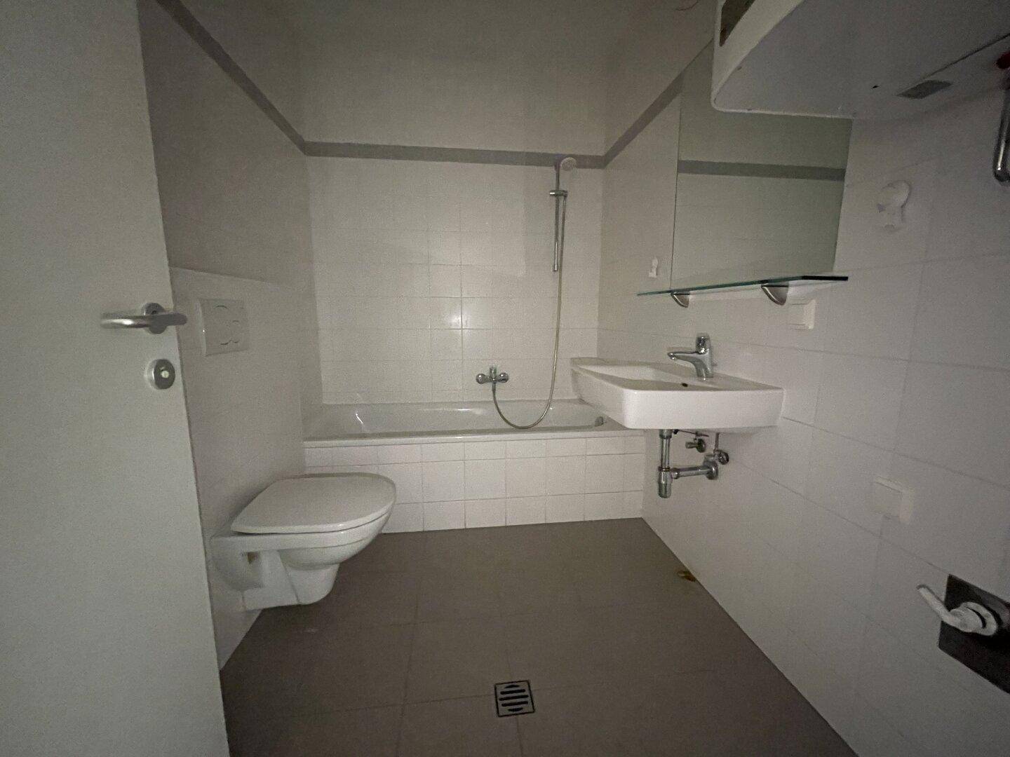 Funktionales Badezimmer mit weißen Wandfliesen, Badewanne und modernem Waschbecken.