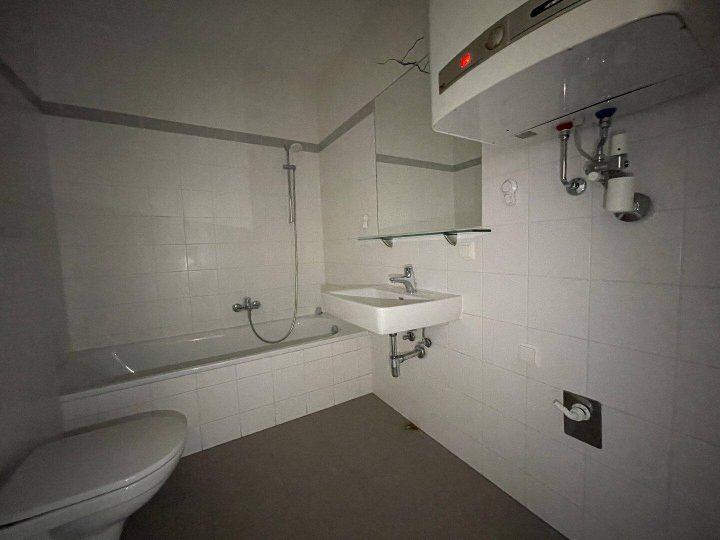 Badezimmer mit Badewanne, Waschbecken, Toilette und einem Warmwasserboiler.