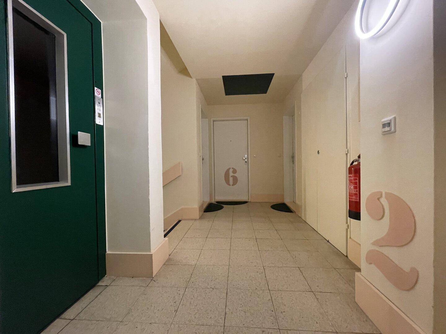 Langer Flur mit Fliesenboden, Aufzugzugang und mehreren Wohnungstüren.