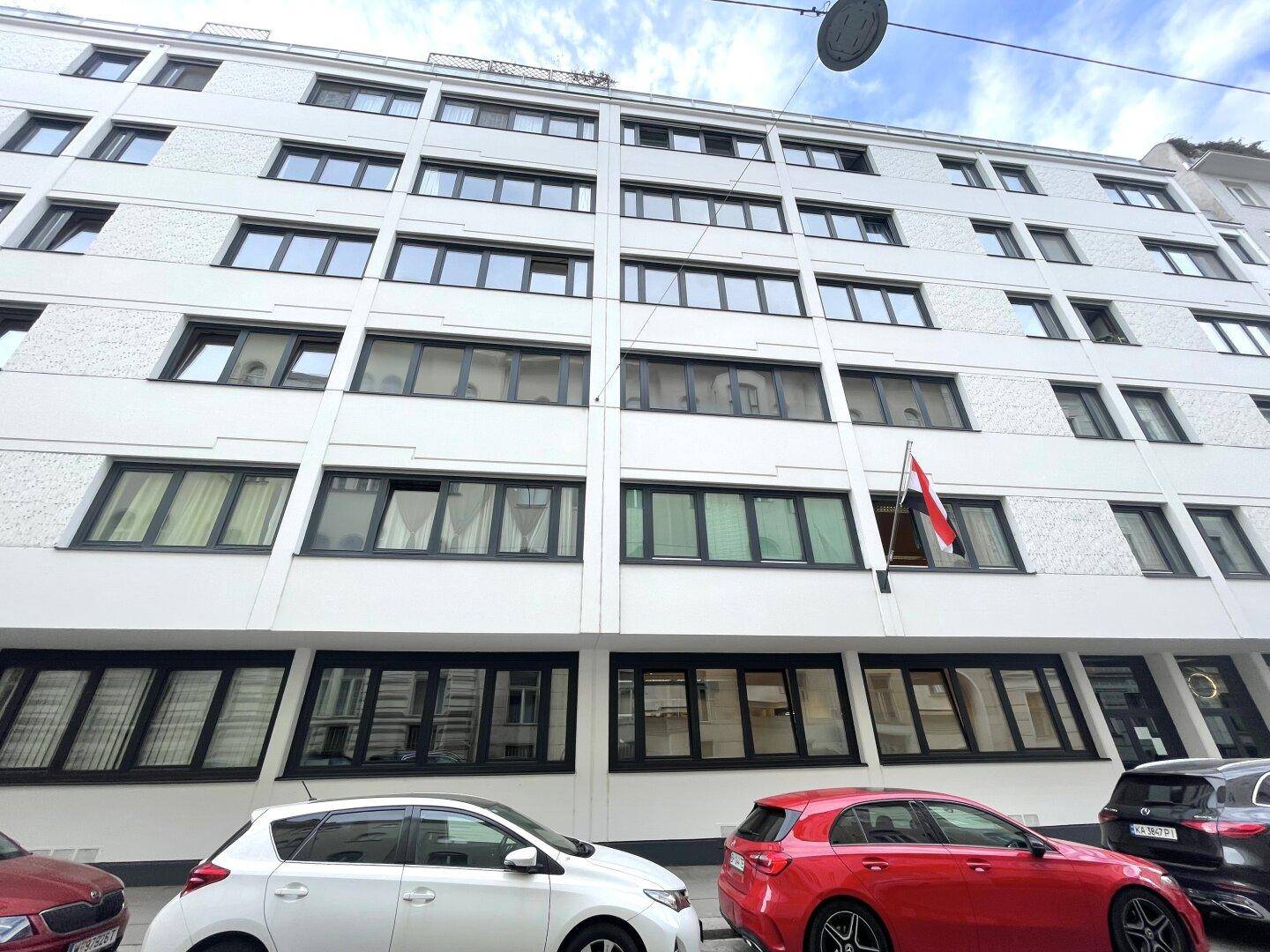 Ansicht der modernen Gebäudefassade mit vielen Fenstern und geparkten Autos davor.