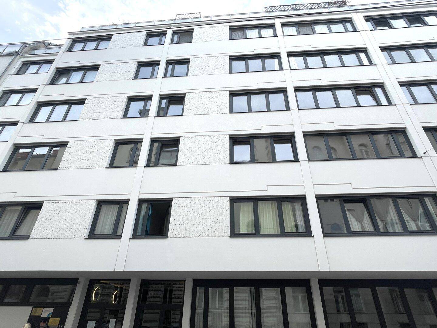 Moderne Gebäudefassade mit vielen Fenstern und einer klaren, strukturierten Architektur in Weiß und Grau.
