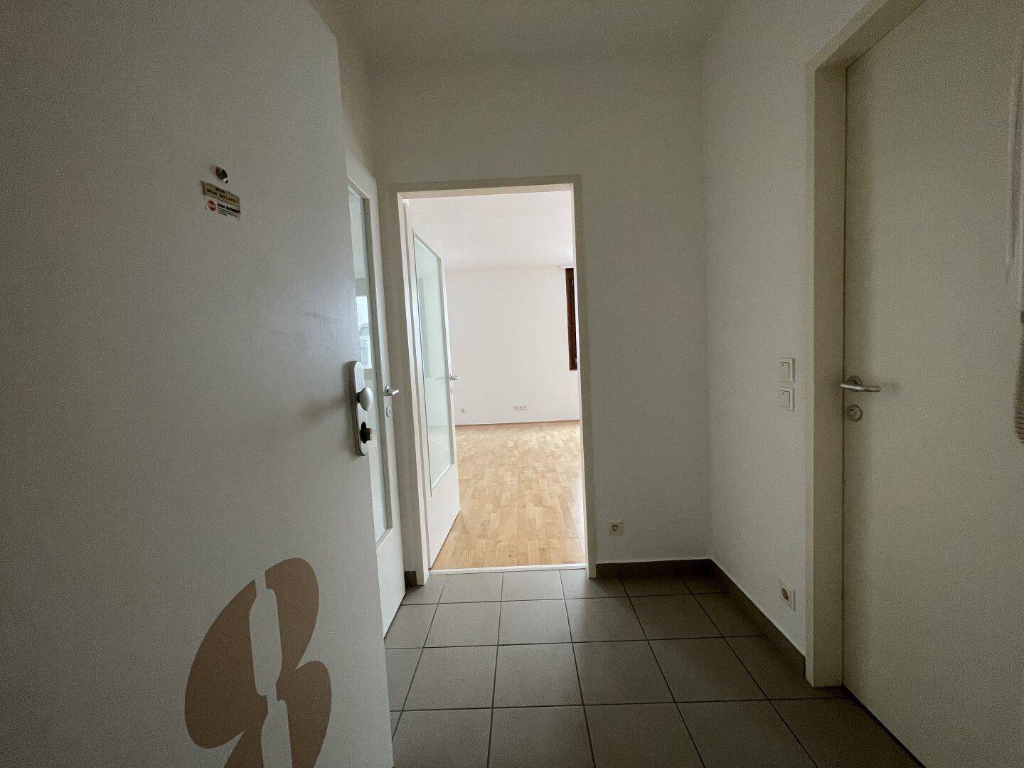 Eingangsbereich der Wohnung mit Fliesenboden und Blick in den angrenzenden Wohnbereich mit Parkett.