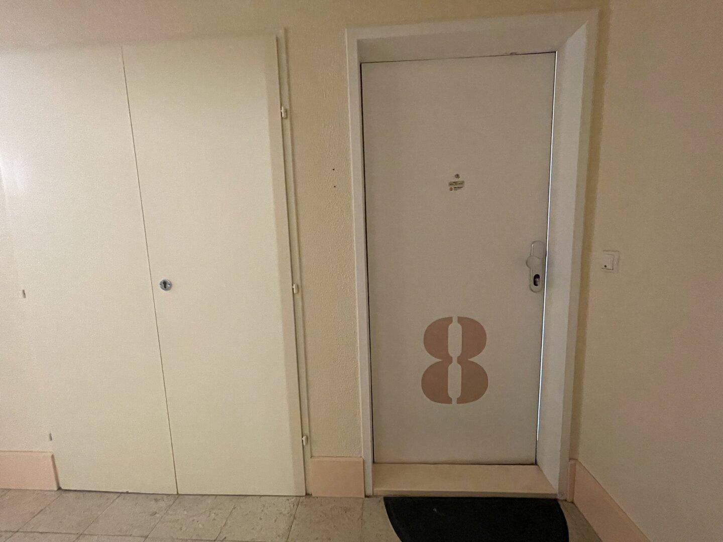 Flur im Mehrfamilienhaus mit einer Wohnungstür, die mit einer großen Nummer versehen ist.