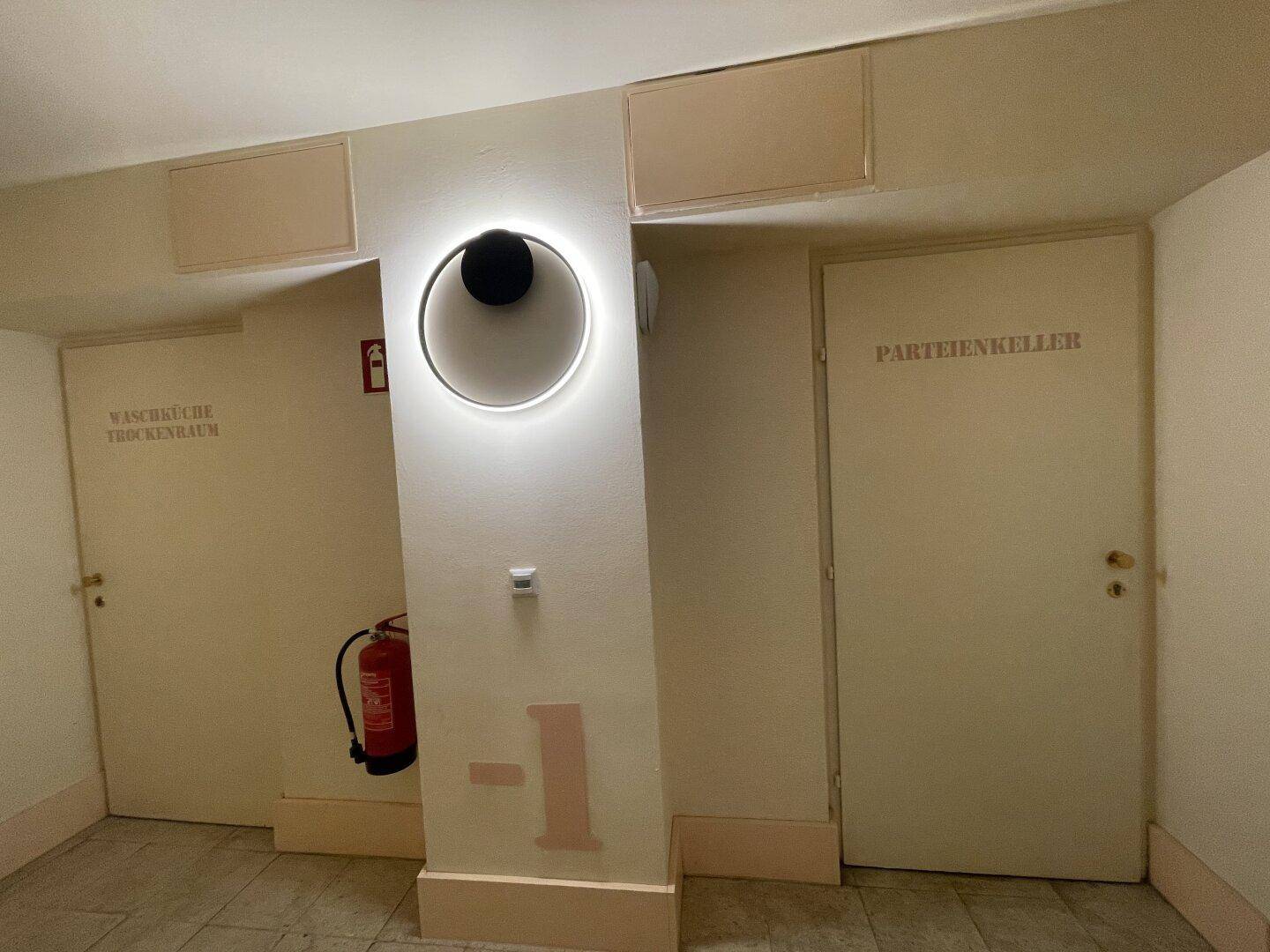 Kellerflur mit Türen zu Gemeinschaftsräumen wie Waschküche und Parteienkeller, beleuchtet von einer modernen Lampe.