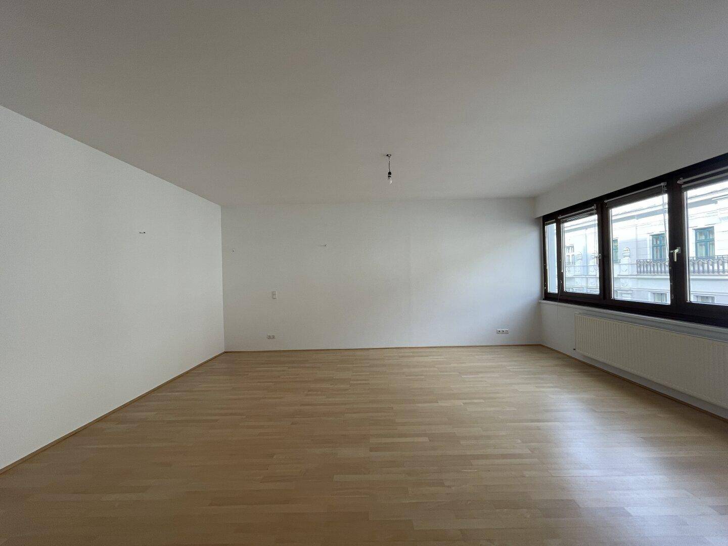 Weitläufiges, leeres Wohnzimmer mit Parkettboden und einer Fensterfront für viel Licht.