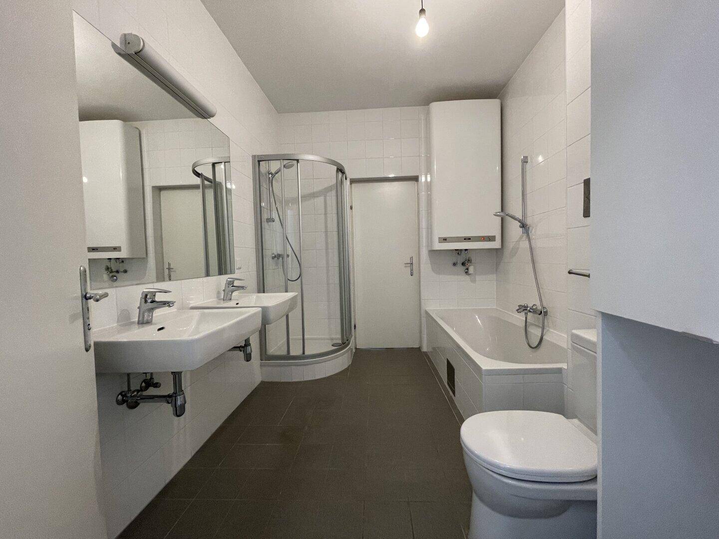 Geräumiges Badezimmer mit Badewanne, Dusche, Doppelwaschbecken und WC, hell gefliest.