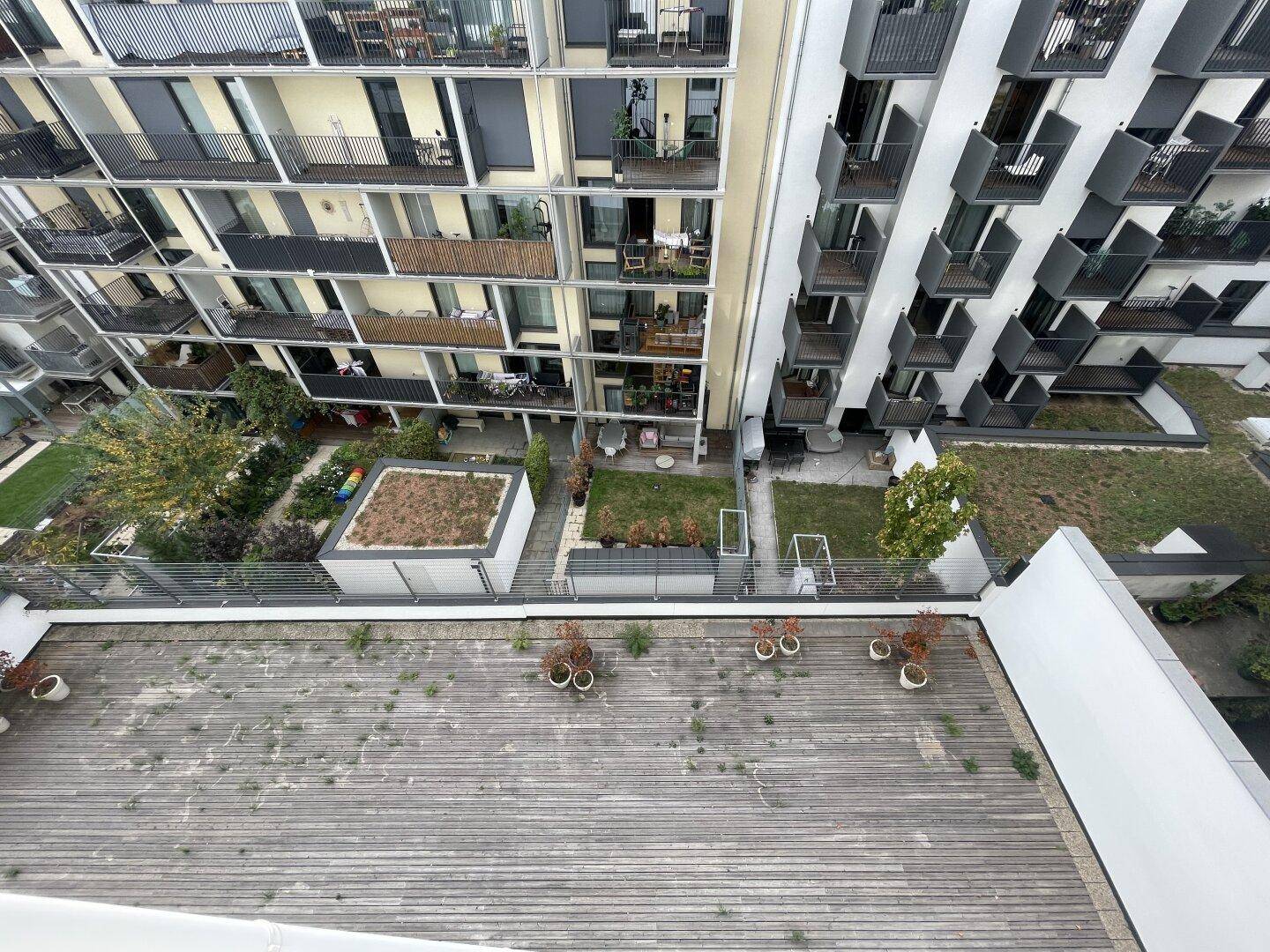 Luftaufnahme eines Innenhofs mit Holzterrasse und umliegenden Wohngebäuden mit Balkonen.