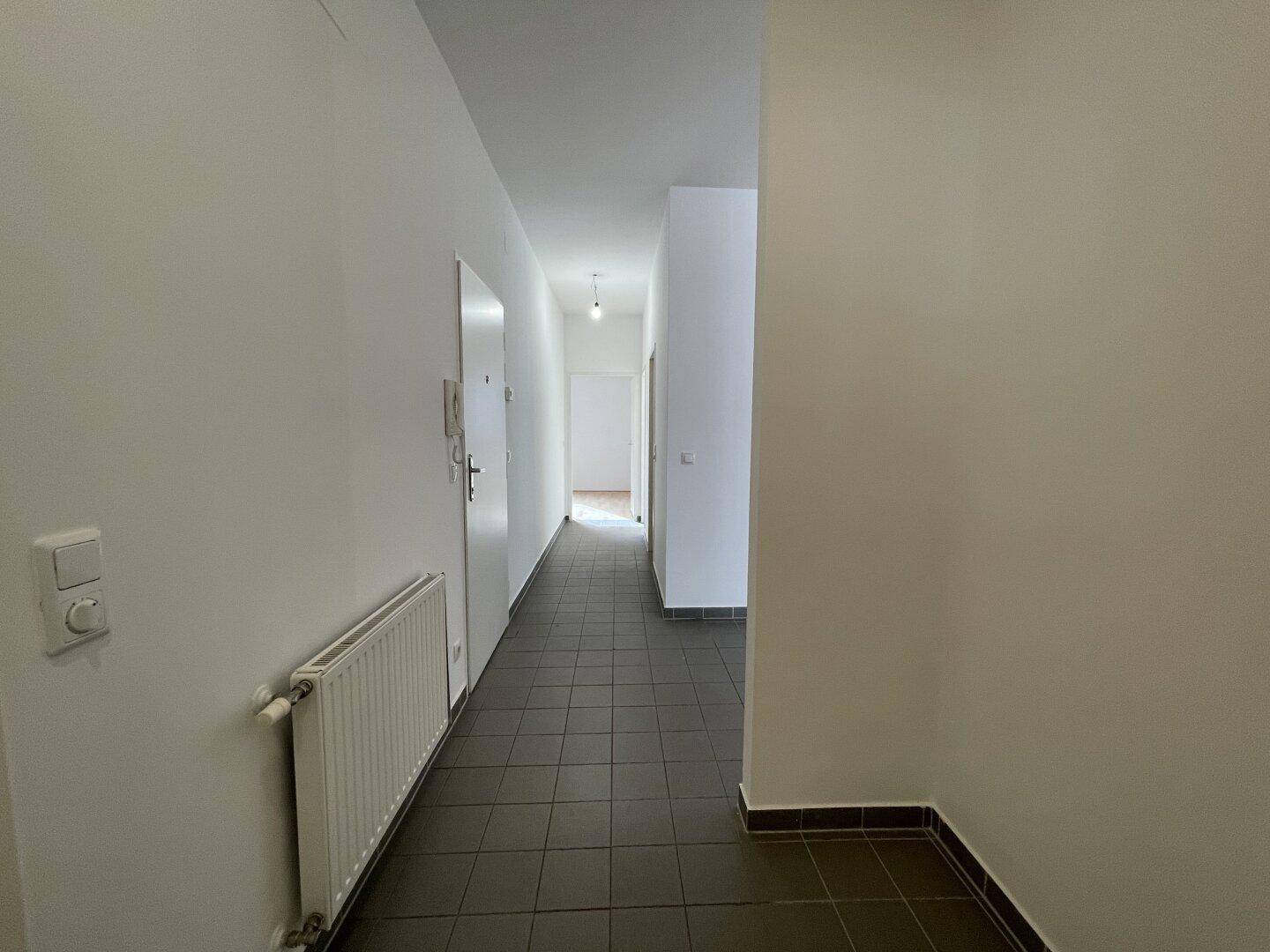 Langer, heller Flur mit Fliesenboden und Heizkörper, der zu den Wohnräumen führt.