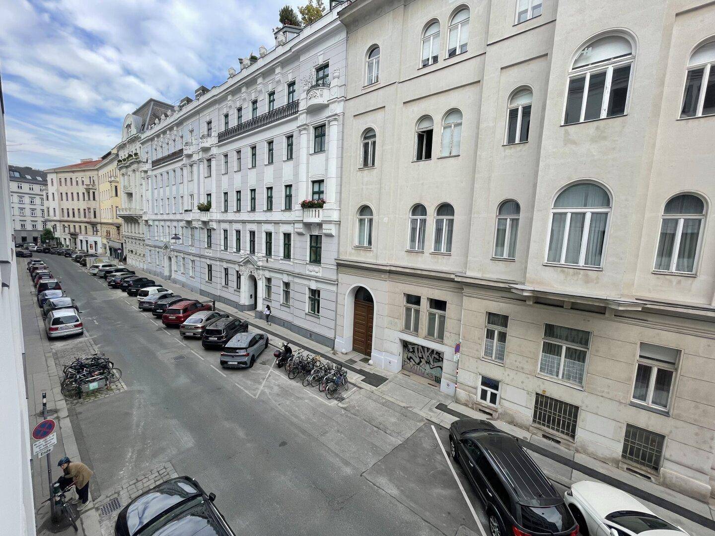 Blick auf eine belebte Stadtstraße mit parkenden Autos und historischen Gebäuden.
