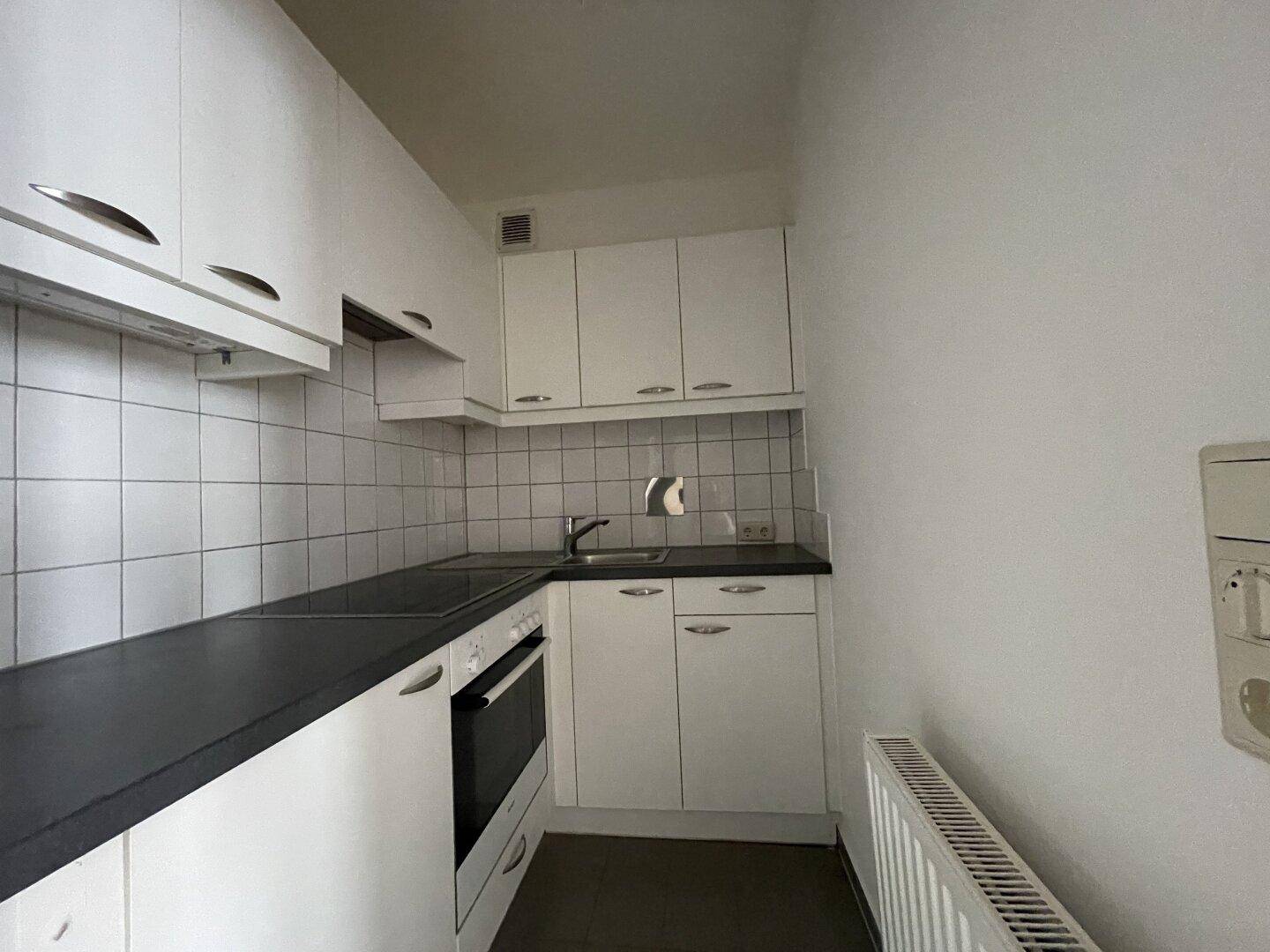Kompakte Küche mit weißen Schränken, dunkler Arbeitsplatte und integrierten Geräten.