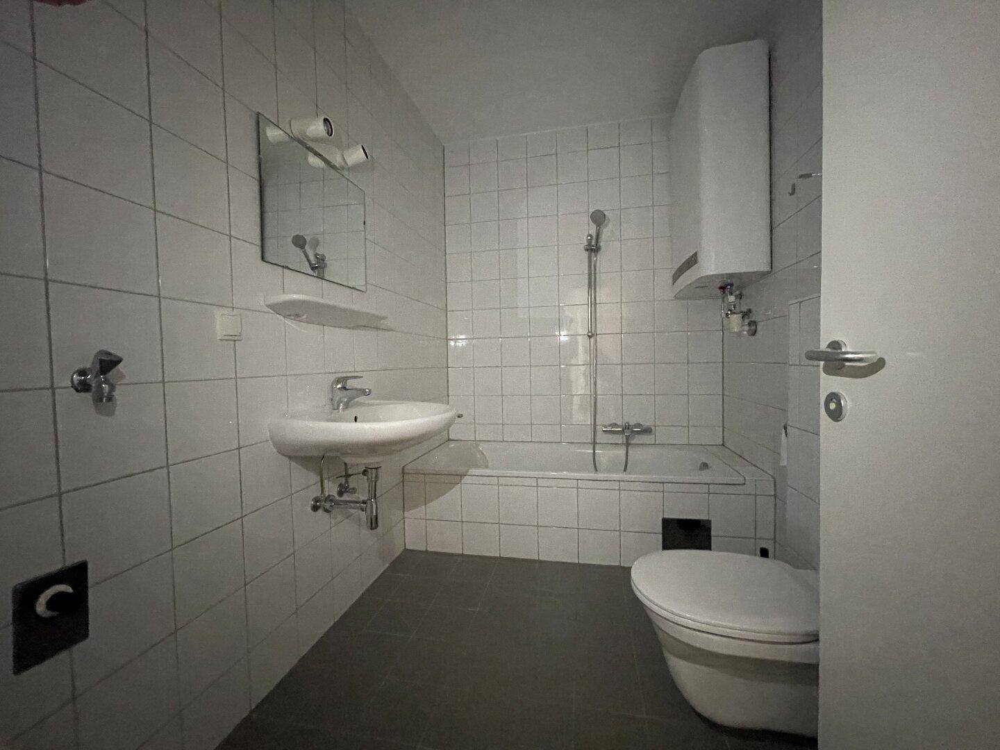 Gefliestes Badezimmer mit Badewanne, WC und Waschbecken in schlichtem Design.