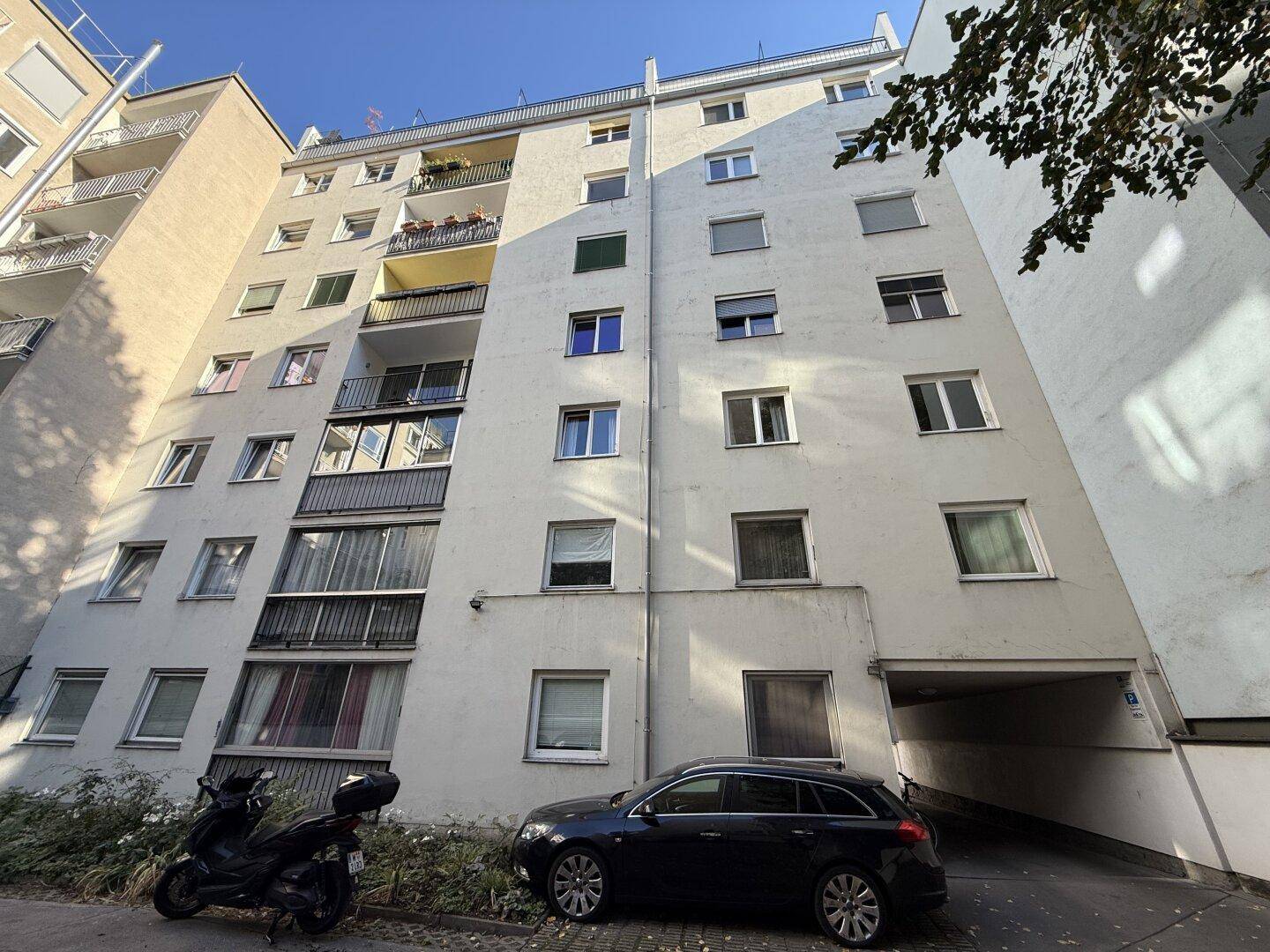 Fassade eines Wohngebäudes mit Balkonen und einem überdachten Eingangsbereich mit Parkmöglichkeit.